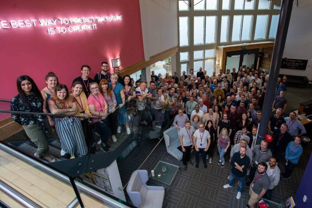 Everyone at Atom bank HQ stood in the lobby looking up and smiling to the camera