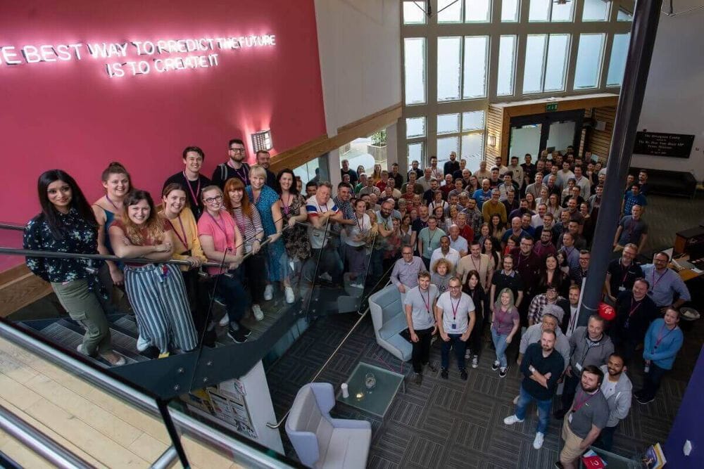Everyone at Atom bank HQ stood in the lobby looking up and smiling to the camera