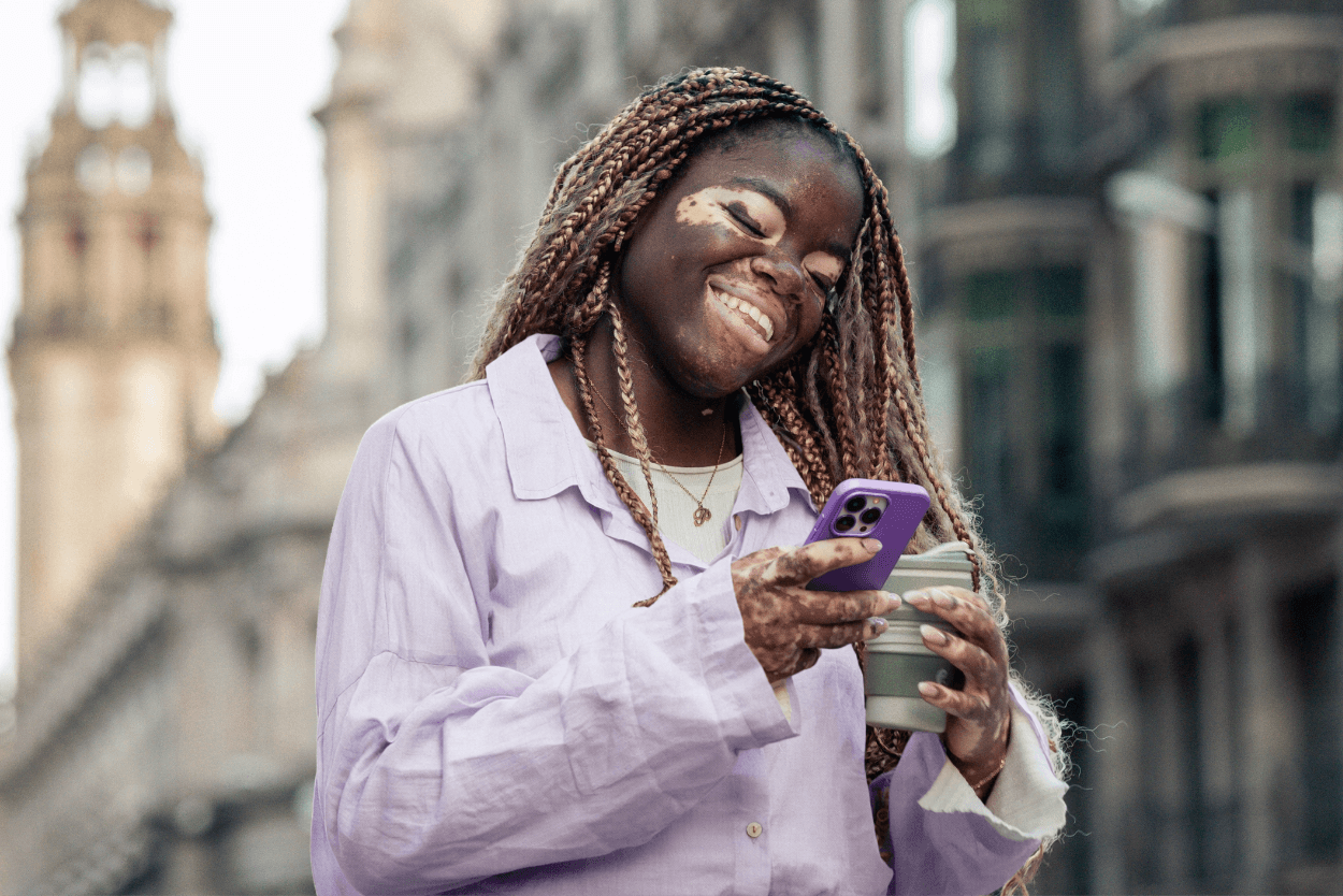 A woman looking at her phone smiling whilst holding a coffee