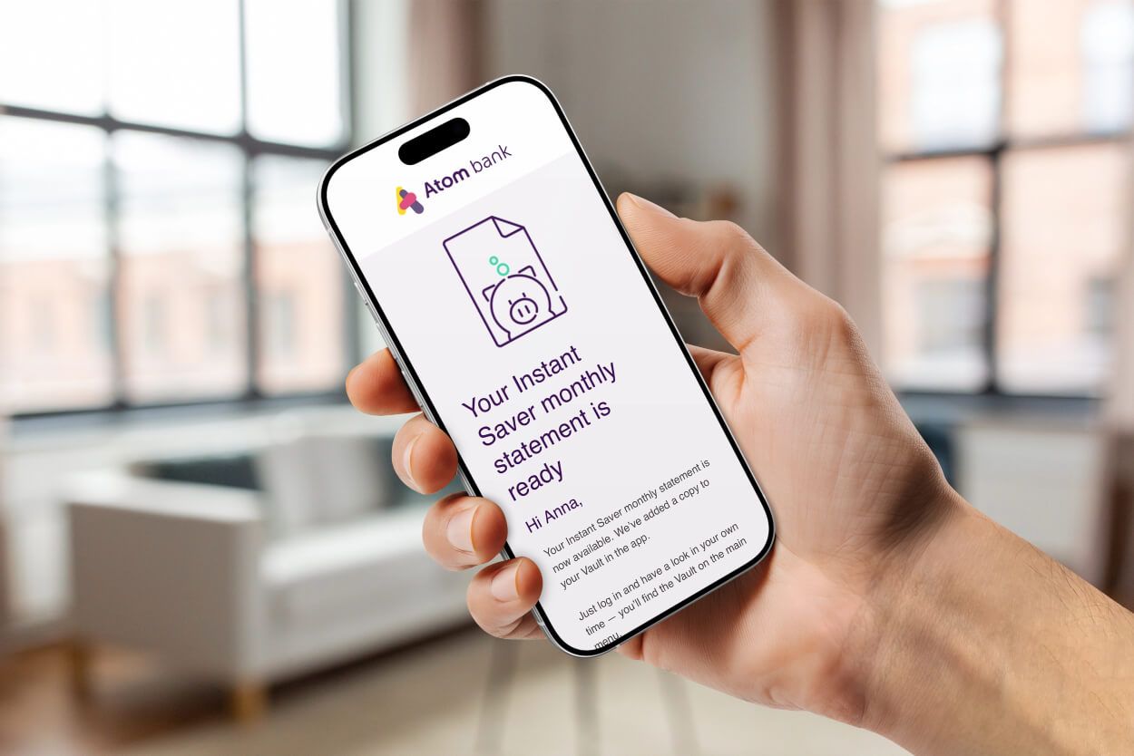 A hand holding a phone displaying an Atom Bank monthly statement