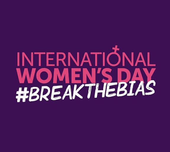 On a purple background, the copy International Woman's Day #BreaktheBias sits in pink and white. The O of Interational has been replaced with the symbol for women