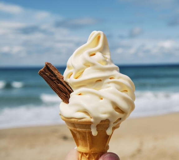 Someone holding a soft serve ice cream cone with a flake at the beach. The copy Atomic numbers Summer 2021
