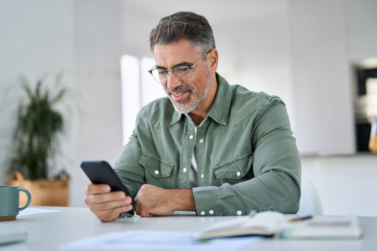 Smiling person wearing glasses and a green overshirt uses their phone