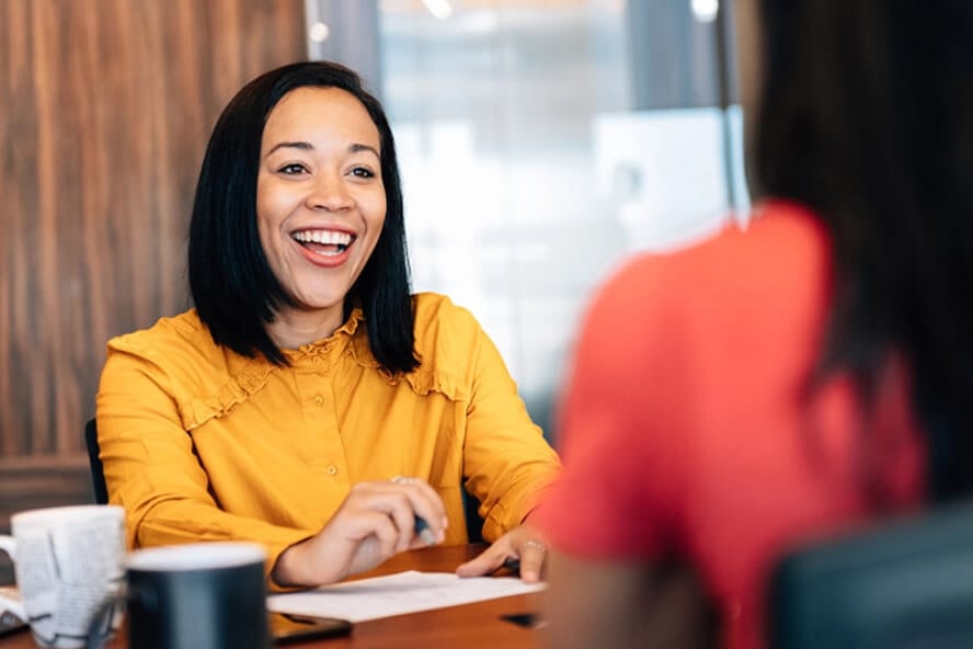 A woman wearing an orange top smiling at someone opposite them