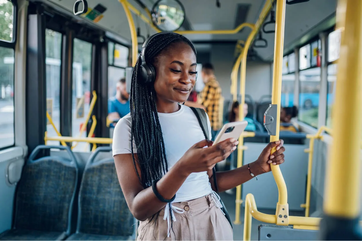 A woman on a bus with headphones on holding a phone