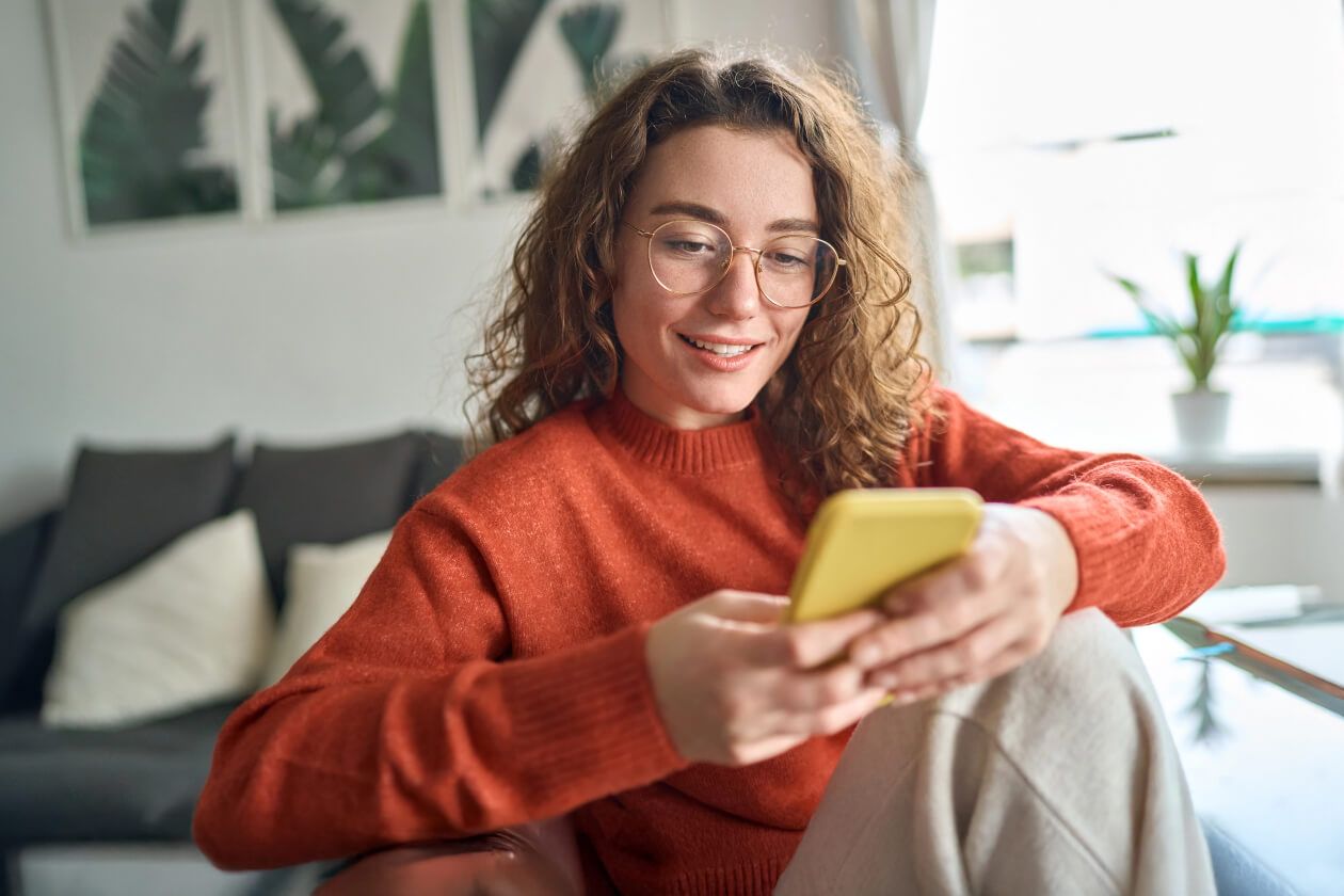 Smiling person wearing glasses and an orange jumper uses their phone