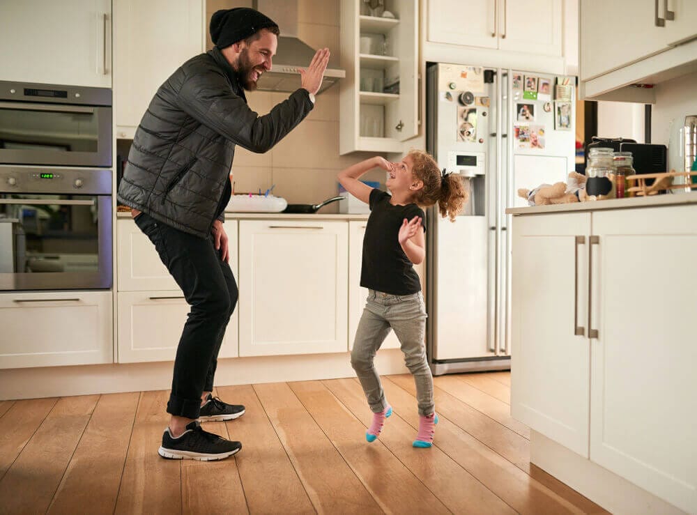 A man is in the kitchen high fiving his daughter