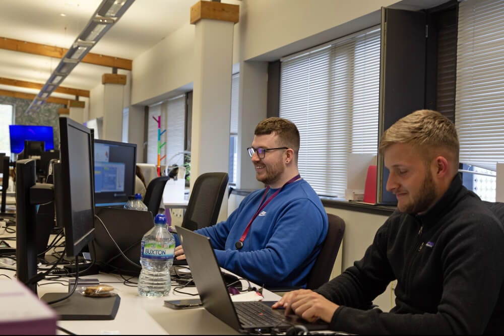 Two men working on a computer and a laptop