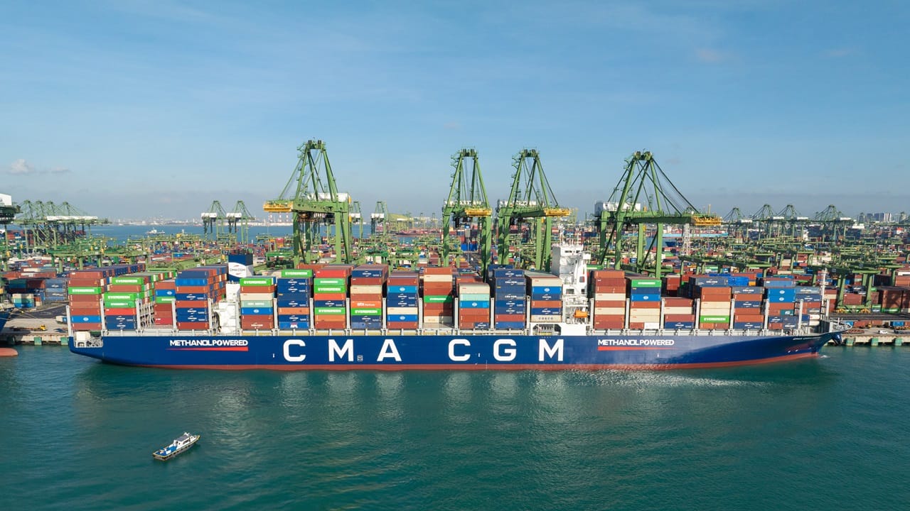 large blue container ship berthed in port with cranes behind