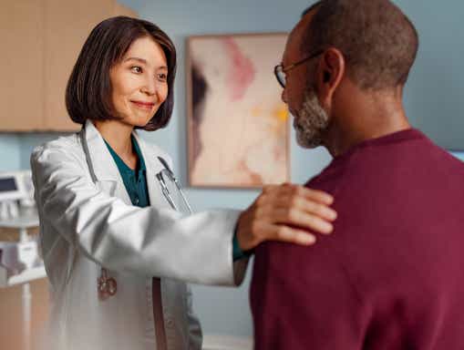 Engagierte Ärztin Eine Ärztin lächelt beruhigend, während sie einem Patienten ihre Hand auf die Schulter legt.