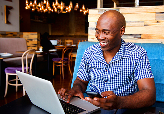 A man sitting at a cafe working on his laptop A man sitting at a cafe, with a smile on his face, working on his laptop