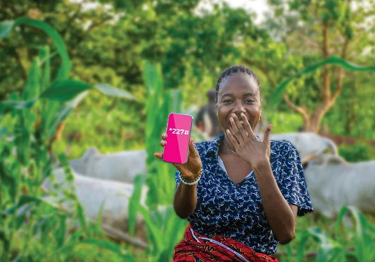 A woman uses her cellphone to access Old Mutual funeral cover services online. A woman wearing a blue dress and sitting in a garden holds up her cellphone.