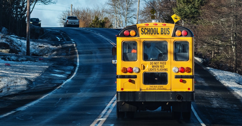 school bus driving on blacktop road on bright winter morning