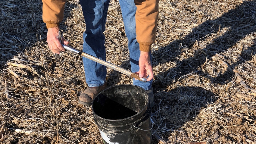 A man holding a soil sample over a black bucket