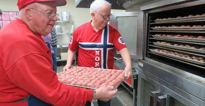 two men putting pan of meatballs into oven