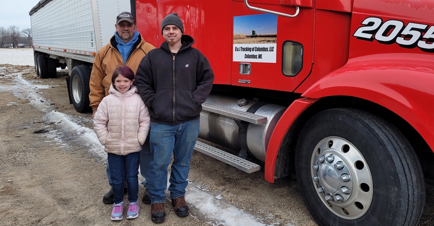 Darren and Jake Schroeder with 7-year-old Gwen in front of red semitruck 