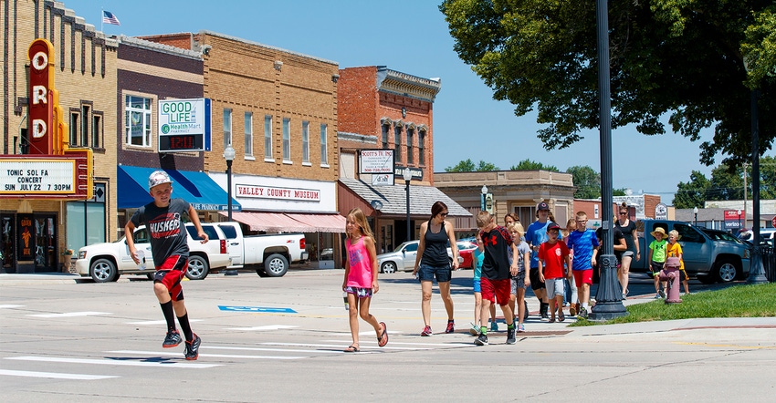 group of kids and adults walking down a sidewalk along a main street in  a downtown