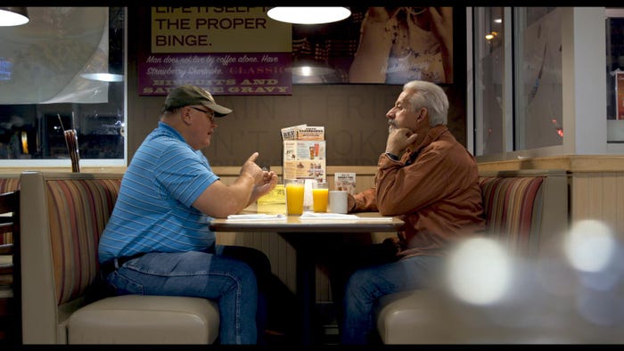 Two men sitting in a booth at a cafe while they have a conversation