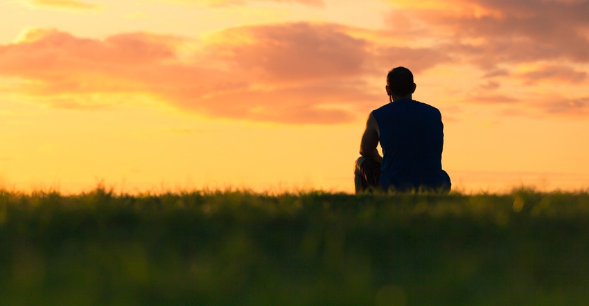 man sitting on grass looking at sunrise
