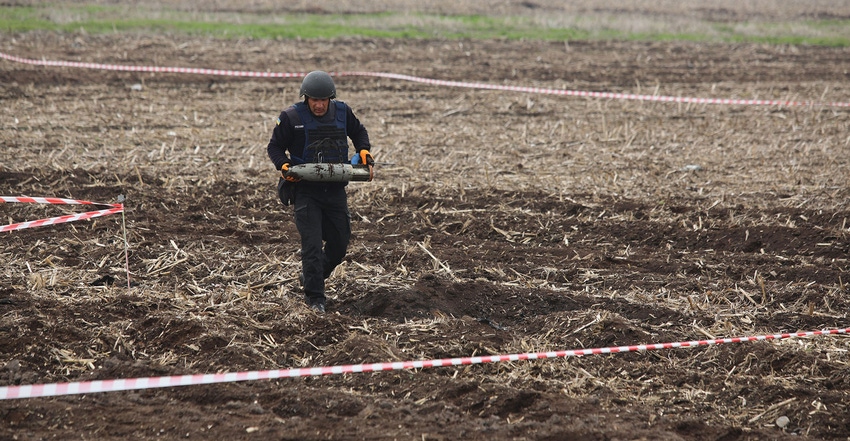 A member of the State Emergency Service of Ukraine carries an unexploded projectile out of a field