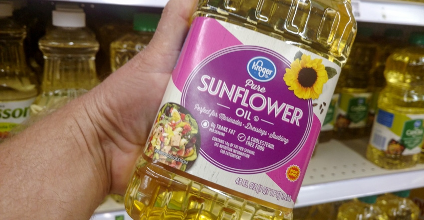 A male hand holding a bottle of Kroger brand sunflower oil A male hand holding a bottle of Kroger brand sunflower oil