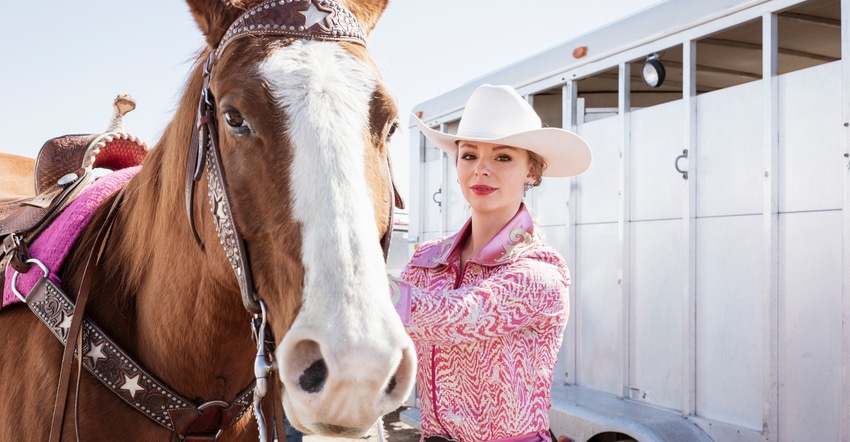 Young cowgirl standing next to horse and trailer