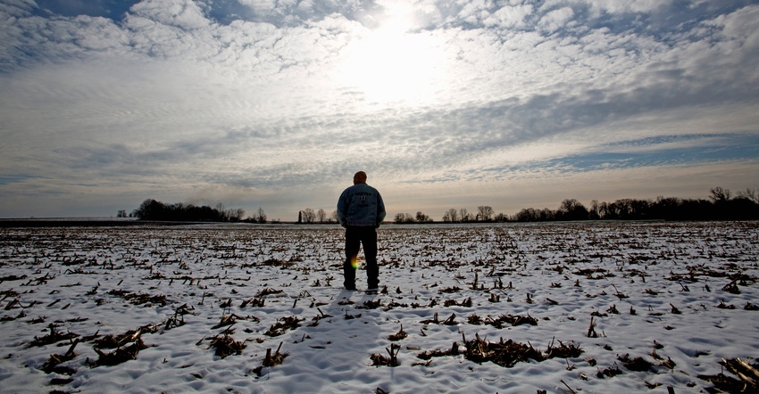 farmer stands out in his snow-dusted cornfield