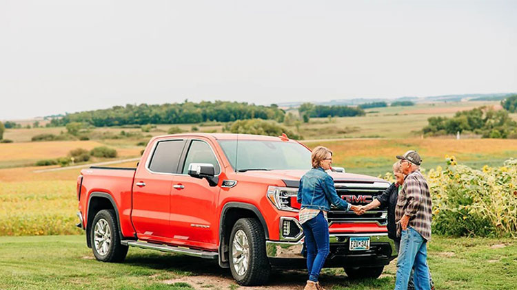 Farmers shake hands in front of red pickup truck