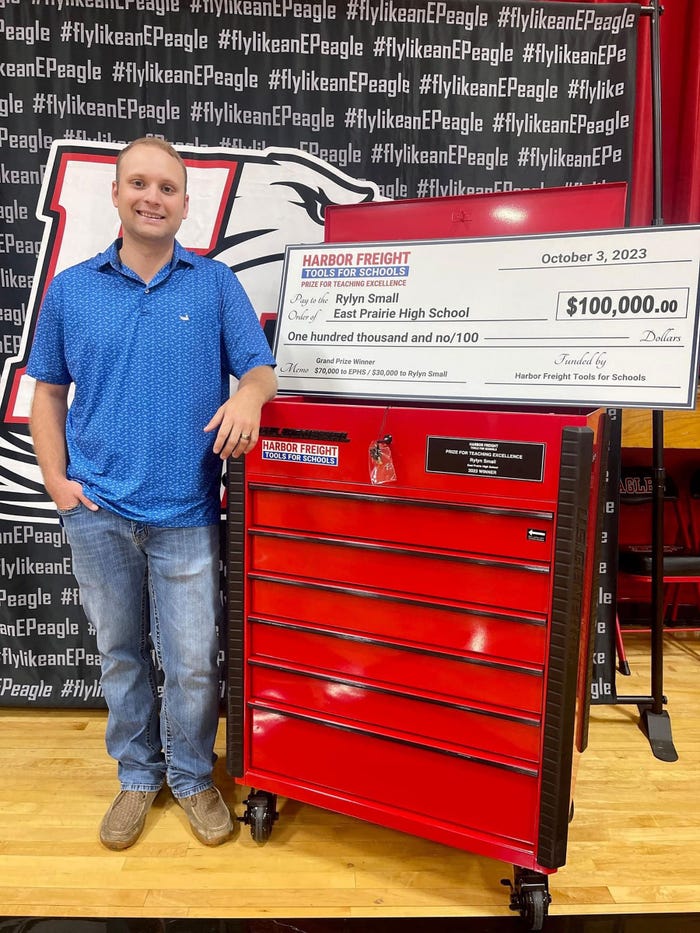 Teacher Rylyn Small smiling and stands next to a large check from 