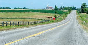 rural country road through farm land with silos, barn and horses