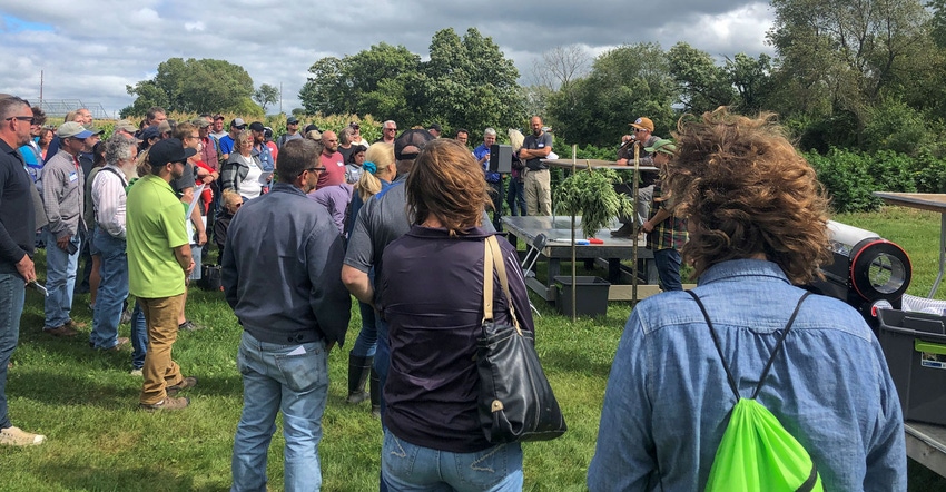 A crowd of people gathered around a man on a platform, listening intently as he holds a microphone to his mouth A crowd of people gathered around a man on a platform, listening intently as he holds a microphone to his mouth