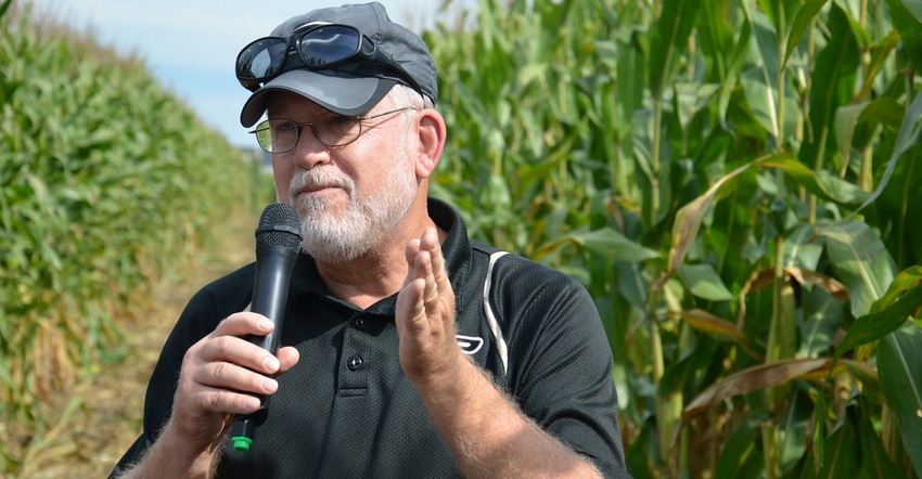Bob Nielsen speaking into microphone in front of cornfield
