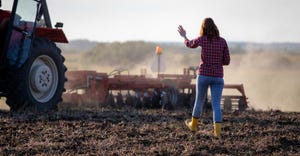 Female farmer walking outdoors towards tractor in field with back to camera