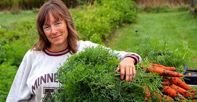 Kristina Beunig, owner of Sunbow farm near Eau Claire, Wisconsin, posing next to carrots on her vegetable farm