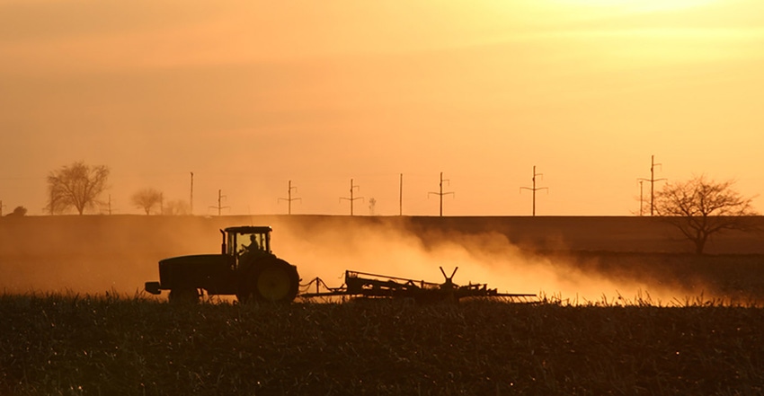 tractor tilling ground at dusk with dust flying.