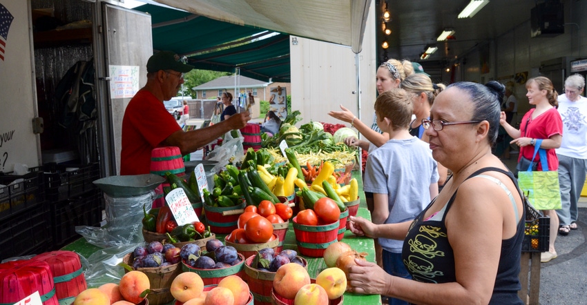 A produce vendor helping customers as they wait in line at a farmers market