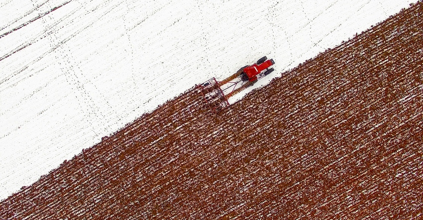 Aerial View of tractor tilling snow covered field in winter