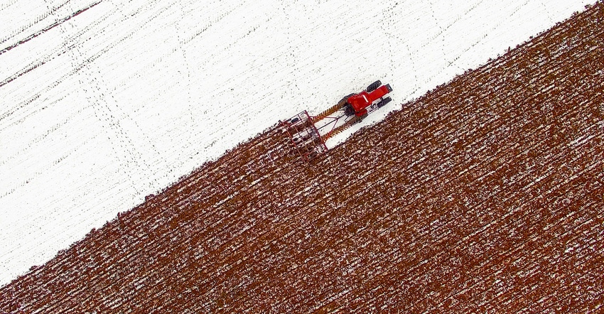 Aerial View of tractor tilling snow covered field in winter Aerial View of tractor tilling snow covered field in winter