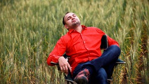 A young man sitting on chair in middle of wheat field