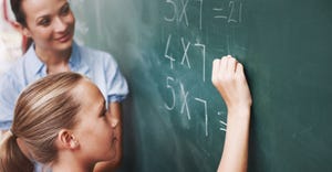 Young student doing math problem on chalkboard with teacher observing