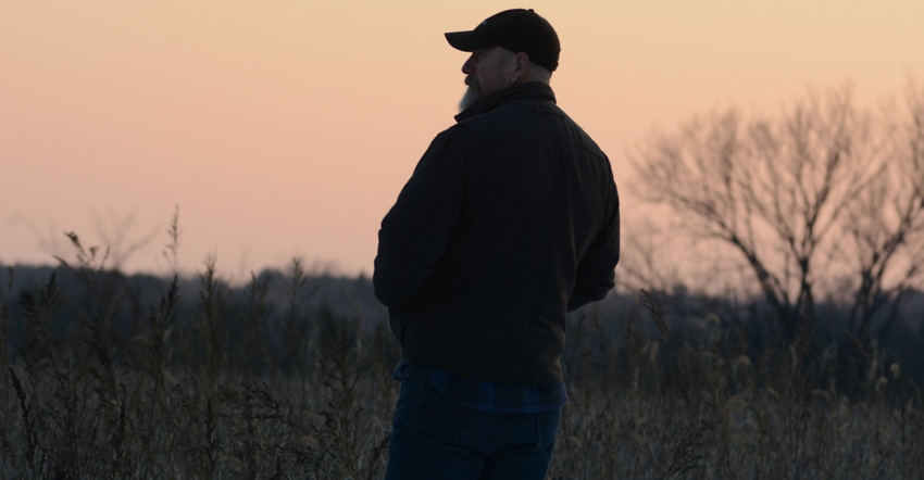 farmer looking off over field at sunset