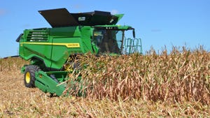 John Deere combine harvesting corn against blue sky