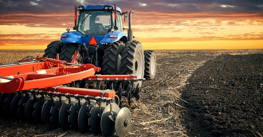 Tractor plowing field on sunset background