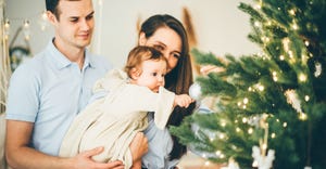 A young couple holding their baby daughter while decorating a Christmas tree