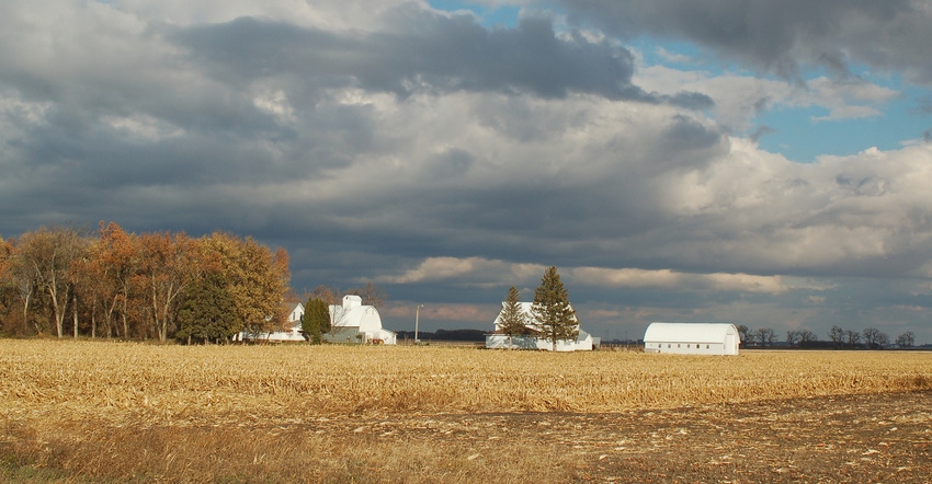 harvested farmland waiting to transition from fall to winter with white house and barns in background