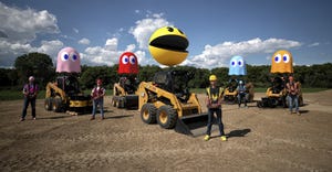 men standing next to skid steers with giant PacMan characters on top 
