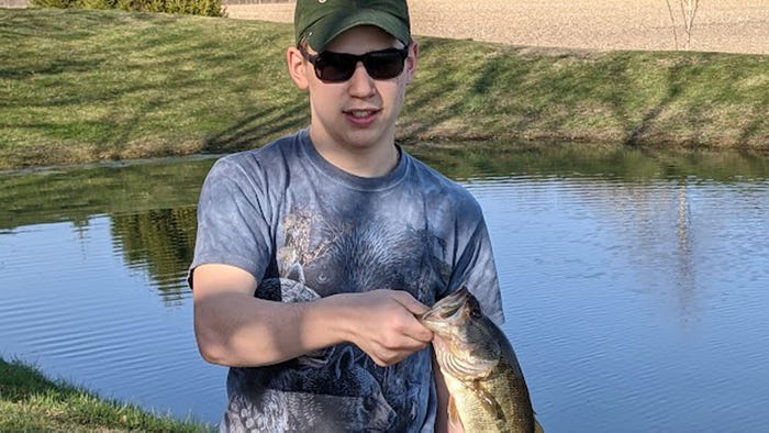 teenage boy holding fish he caught by the mouth