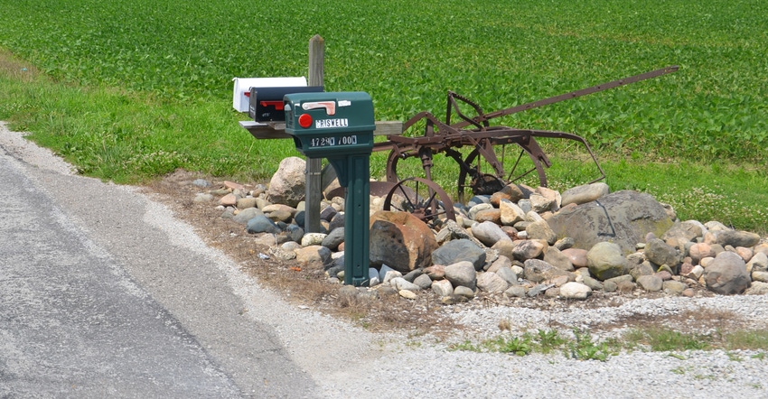 old plow displayed in rocks next to three mailboxes along rural road