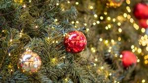 A close up of a red Christmas ornament handing on a tree with lights