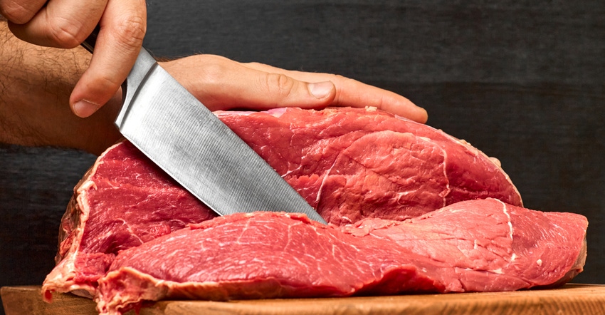 Closeup of hand cutting a beef meat with a knife on a black background